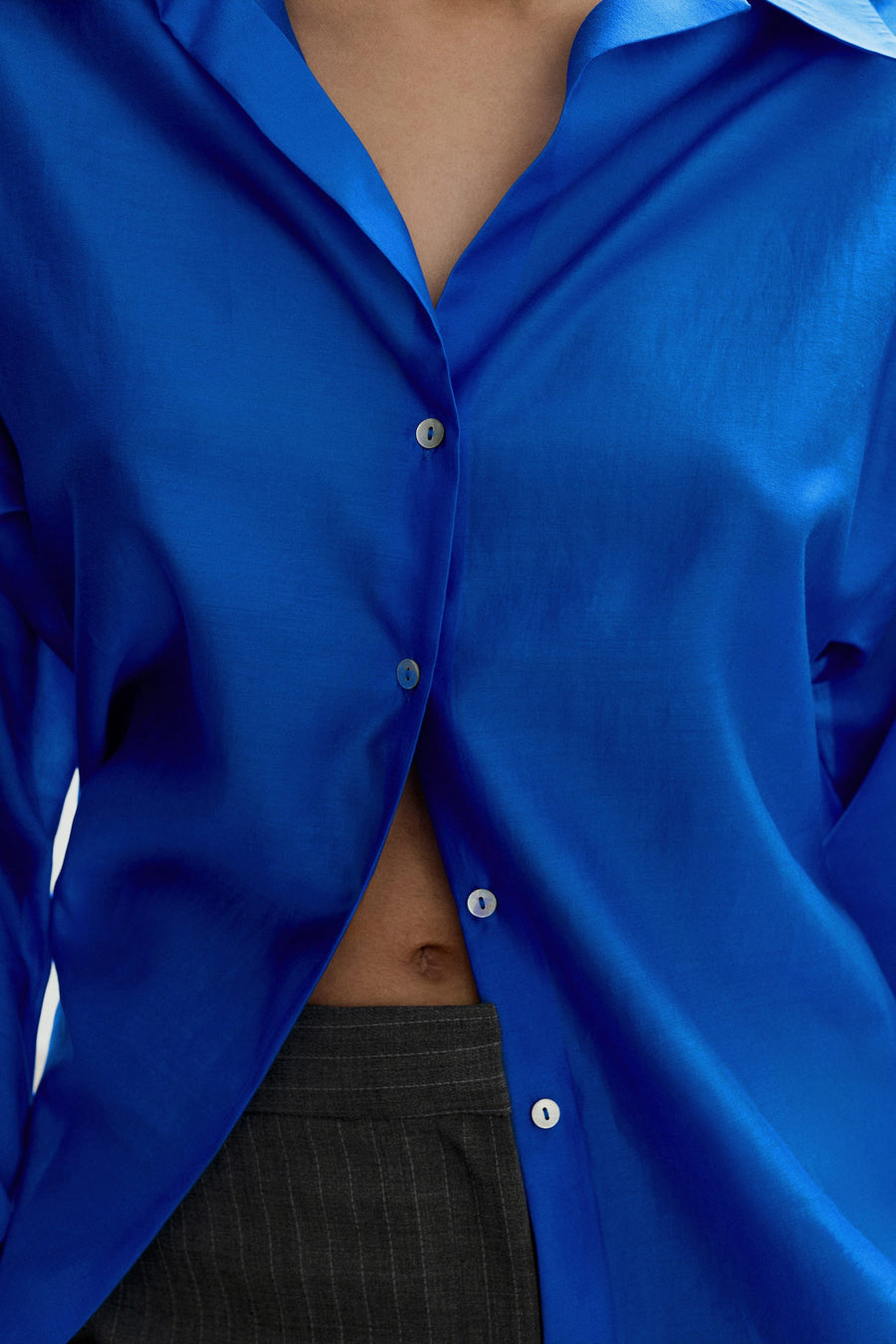 Blauwe blouse met lange mouwen van MANGO, met parelmoeren knopen en een gestreepte broek zichtbaar.