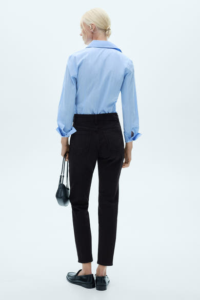 Zwarte mom jeans van MANGO, gedragen met een lichtblauw gestreept overhemd en zwarte loafers.