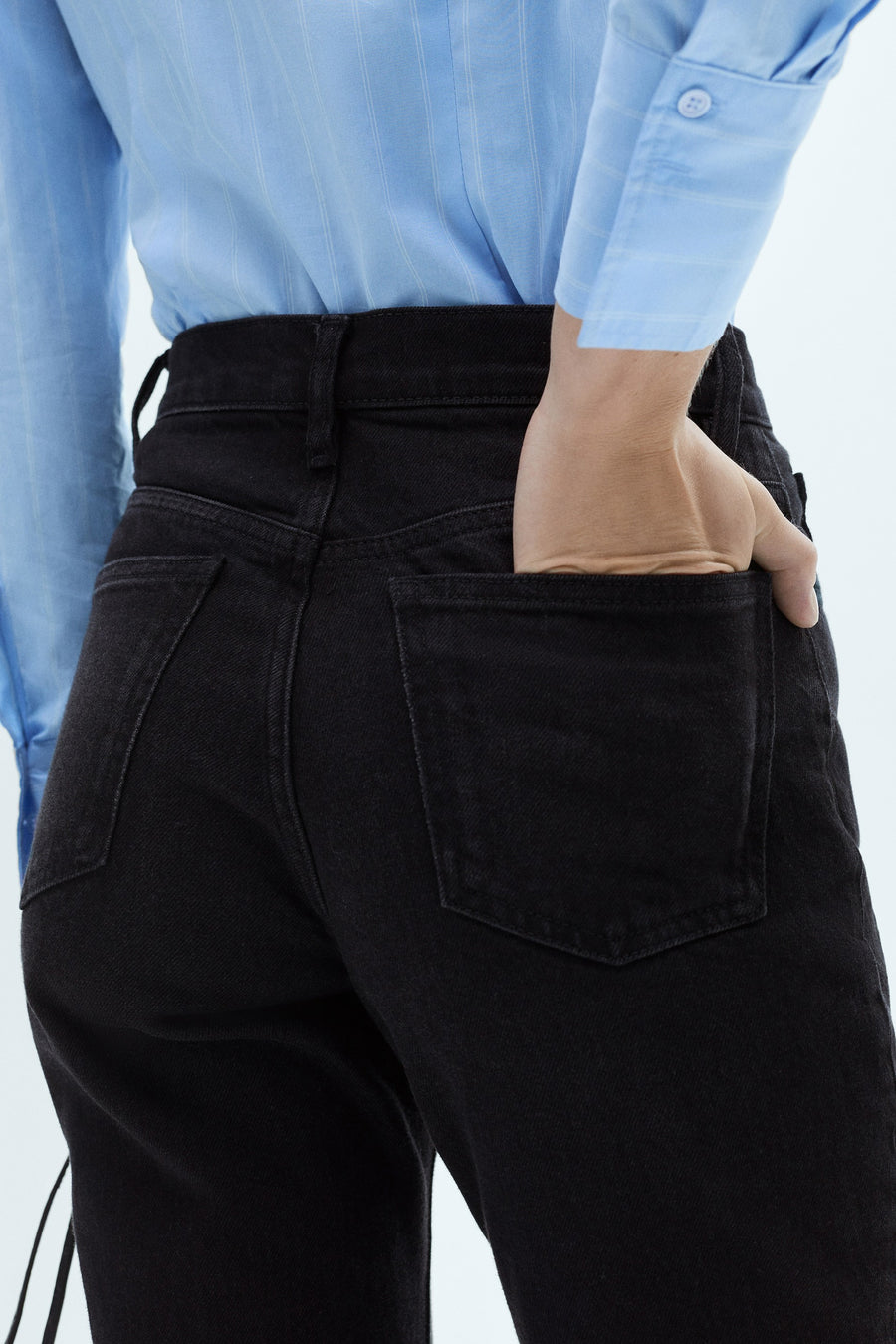 Zwarte 'Mom' jeans van MANGO, met een hand in de achterzak, gedragen met een blauw gestreept overhemd.