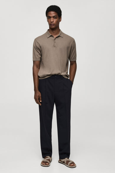 Pantalon bleu de MANGO, porté avec un polo marron clair et des sandales croisées.
