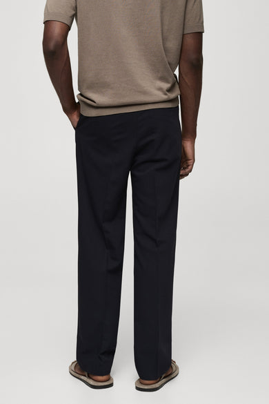 Pantalon bleu de MANGO, coupe droite et jambes larges, porté avec un t-shirt marron clair et des sandales.