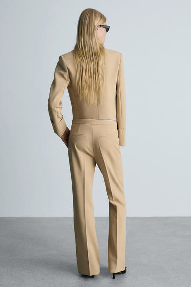 Bruine broek van MANGO, rechte pasvorm, gedragen met een bijpassende blazer en zwarte hakken, achterzicht.