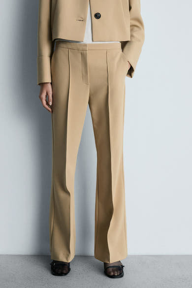 Bruine broek van MANGO met centrale plooien, gedragen met een korte beige blazer en zwarte sandalen.