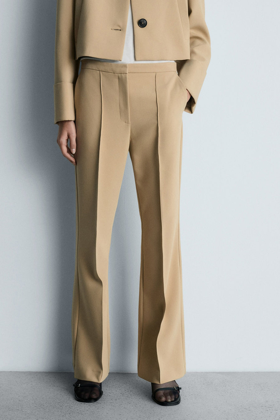 Bruine broek van MANGO met centrale plooien, gedragen met een korte beige blazer en zwarte sandalen.