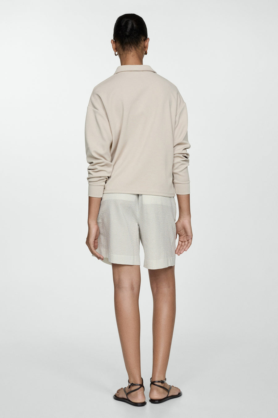Short écru de MANGO, rayé, porté avec un haut beige à manches longues et des sandales à lanières.