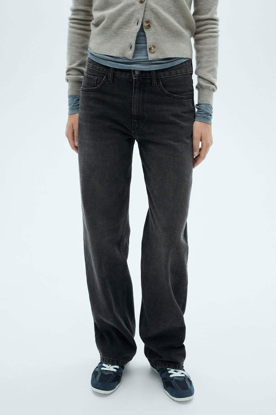 Rechte donkergrijze jeans van MANGO, relaxed fit, gedragen met een beige trui en blauwe sportschoenen.