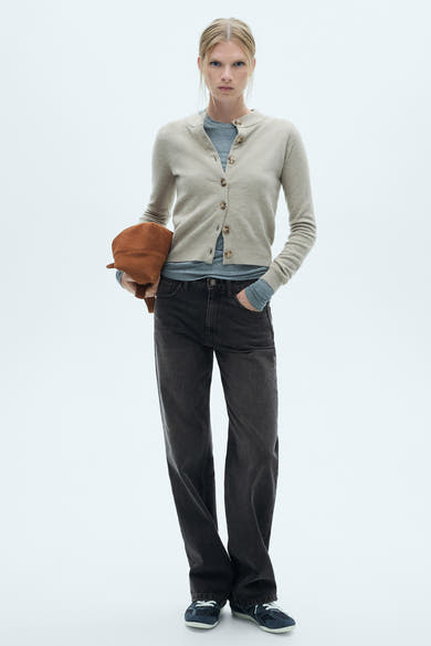 Rechte donkergrijze jeans van MANGO, gedragen met een beige vest, een grijs T-shirt en marineblauwe sneakers.