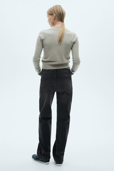Jeans droit gris foncé de MANGO, coupe décontractée, portés avec un pull beige et des chaussures de sport bleues.
