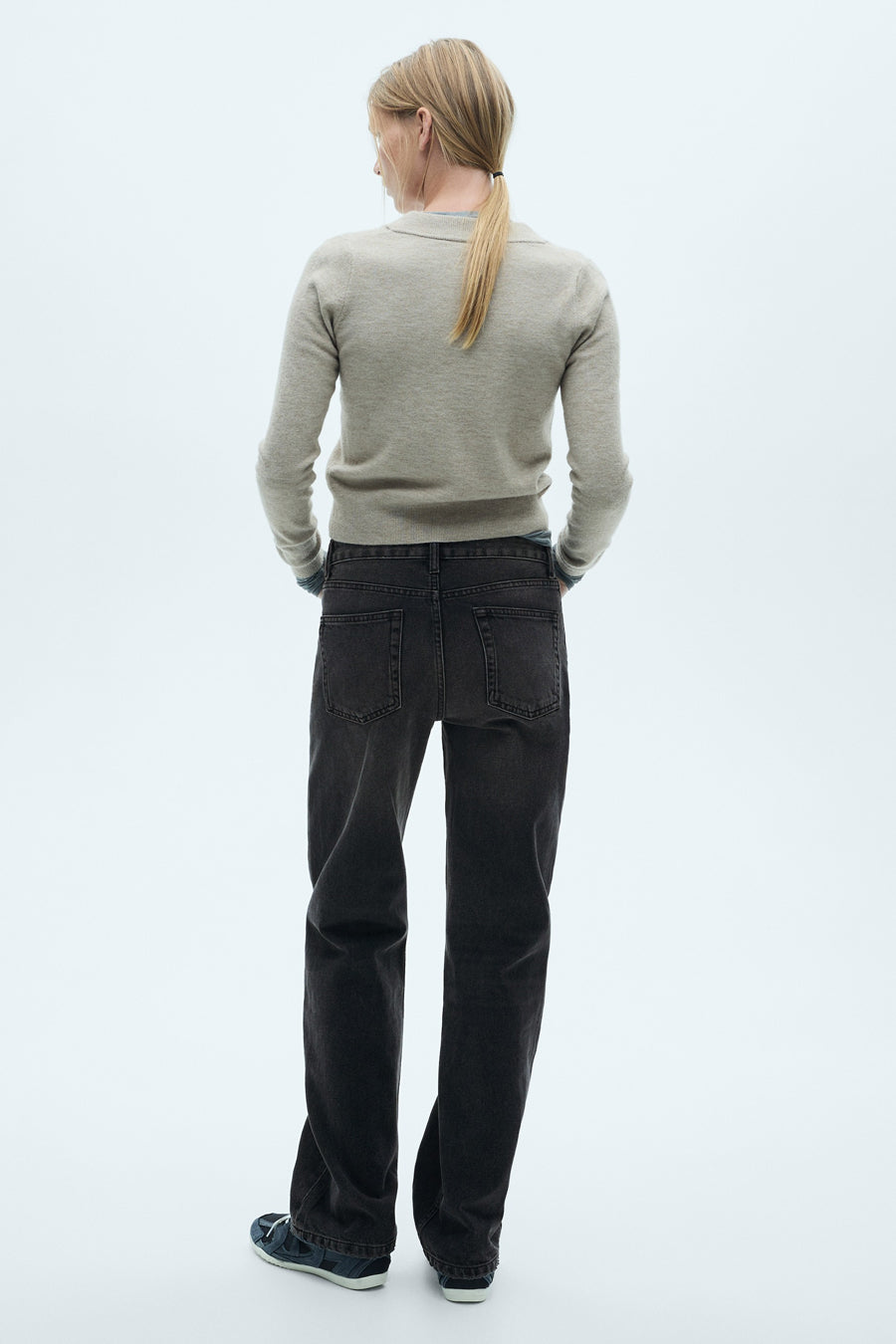 Jeans droit gris foncé de MANGO, coupe décontractée, portés avec un pull beige et des chaussures de sport bleues.