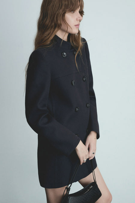 Veste longue bleue par MANGO, avec une coupe croisée et des boutons noirs, portée avec un sac noir.