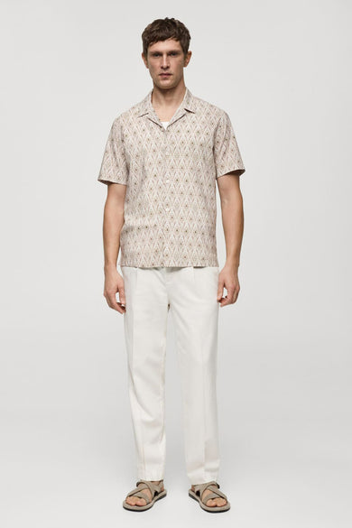Chemise beige à manches courtes de MANGO, avec un motif losanges et portée avec un pantalon blanc.