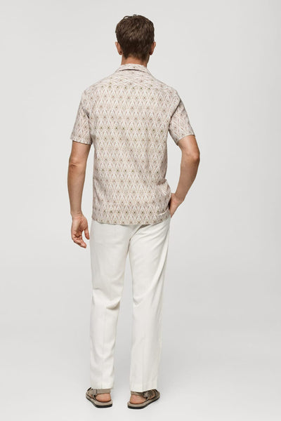 Chemise beige à manches courtes de MANGO, motif losanges, portée avec un pantalon blanc et des sandales.