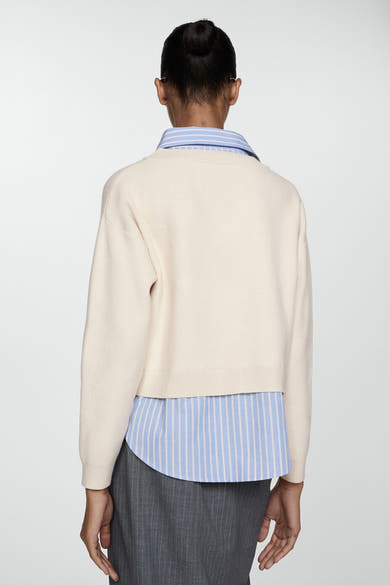 Beige V-hals trui van MANGO, gedragen over een blauw-wit gestreept overhemd, met een grijze rok.