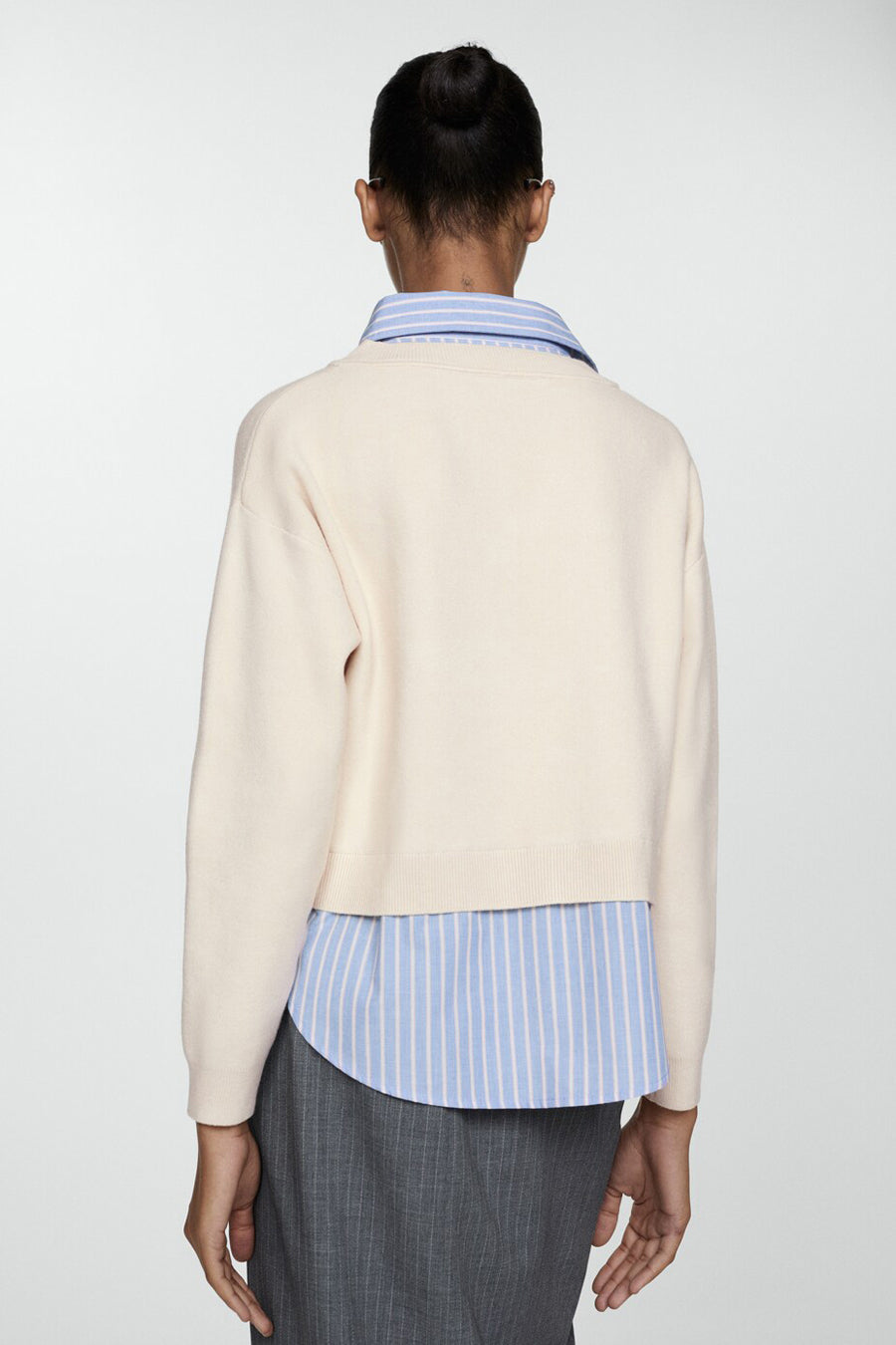 Beige V-hals trui van MANGO, gedragen over een blauw-wit gestreept overhemd, met een grijze rok.