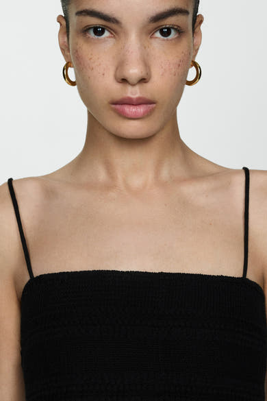 Robe noire de MANGO, coupe droite, fines bretelles, motif texturé, portée avec des boucles d'oreilles dorées.