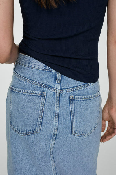 Mid blue denim skirt with back pockets and visible stitching, worn with a dark navy ribbed top, back view close-up