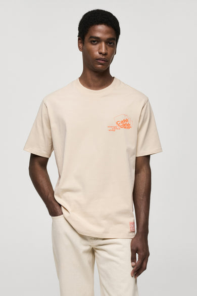 T-shirt à manches courtes beige de MANGO, avec un imprimé graphique orange sur le devant, porté avec un pantalon assorti.