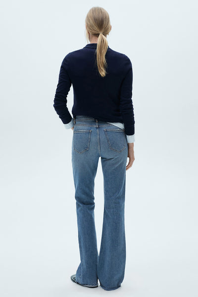 Middelblauwe flared jeans van MANGO, gedragen met een marineblauwe trui en een wit overhemd.