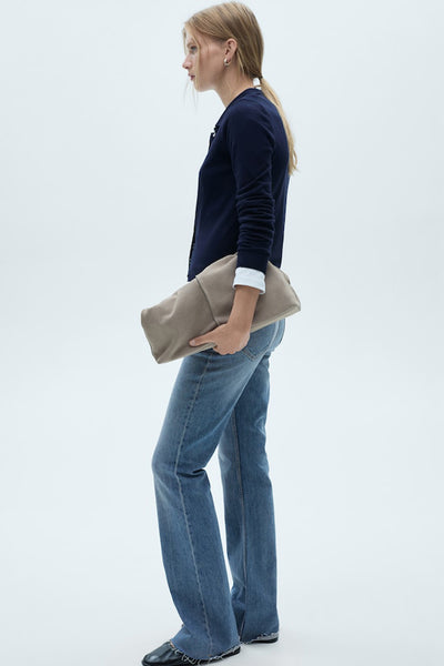 Middelblauwe flared jeans van MANGO, gedragen met een marineblauwe cardigan en een beige clutch.