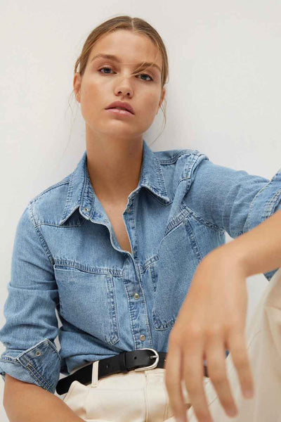 Blue denim long-sleeve shirt with button-down front and chest pockets, worn with rolled sleeves and black belt, side view.