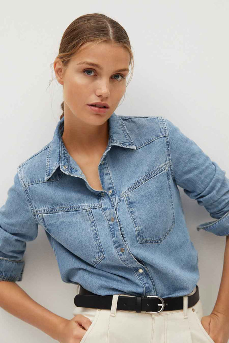 Blue denim long-sleeve shirt with chest pockets and button-down front, worn with white pants and black belt, front view