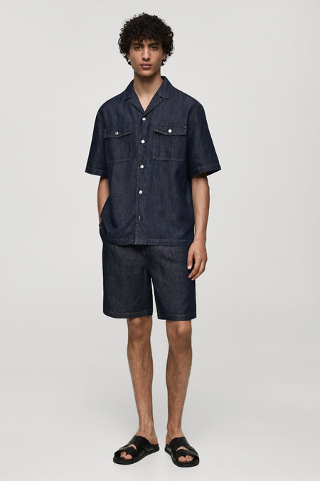 Korte spijkerbroek in middinblauw van MANGO, gedragen met een bijpassend overhemd en zwarte leren sandalen.