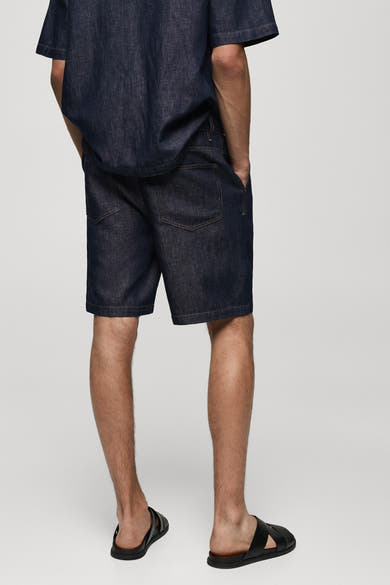 Short en denim bleu moyen de MANGO, vue de dos, porté avec des sandales noires.
