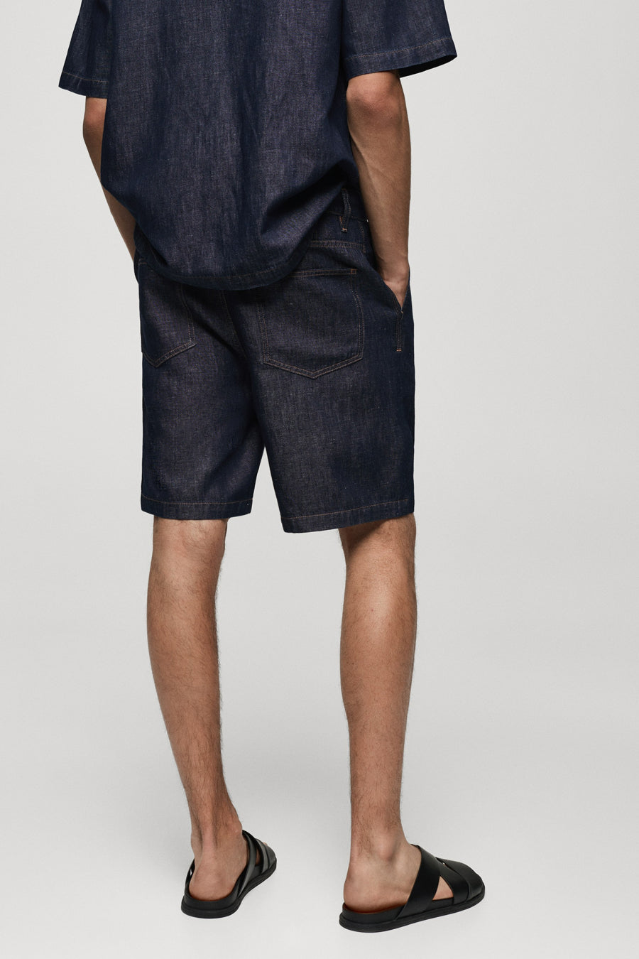 Short en denim bleu moyen de MANGO, vue de dos, porté avec des sandales noires.
