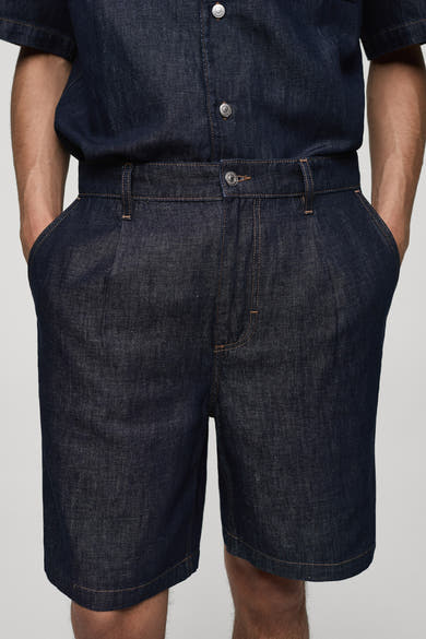 Short en denim bleu moyen de MANGO, avec des plis sur le devant et une ceinture intégrée.
