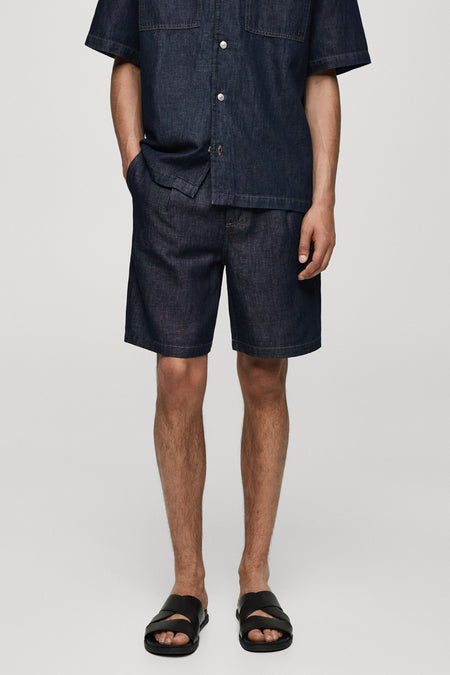 Korte spijkerbroek in middinblauw van MANGO, gedragen met een bijpassend overhemd en zwarte kruissandalen.