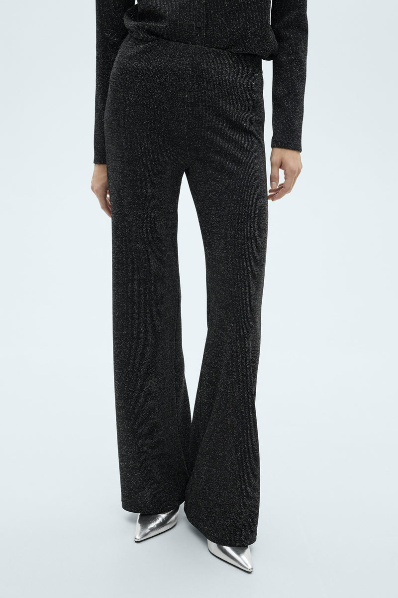 Grijze broek, van MANGO, met een uitlopende pasvorm en een glanzende textuur, gedragen met zilveren schoenen.