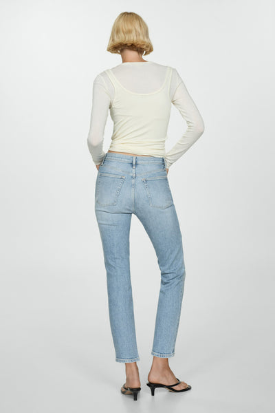 Jean slim en denim bleu clair de MANGO, porté avec un t-shirt à manches longues écru et des mules noires.