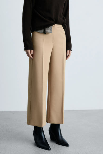 Beige broek van MANGO, wijde pasvorm, gedragen met een bruine trui en zwarte enkellaarsjes.