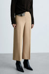 Beige broek van MANGO, wijde pasvorm, gedragen met een bruine trui en zwarte enkellaarsjes.