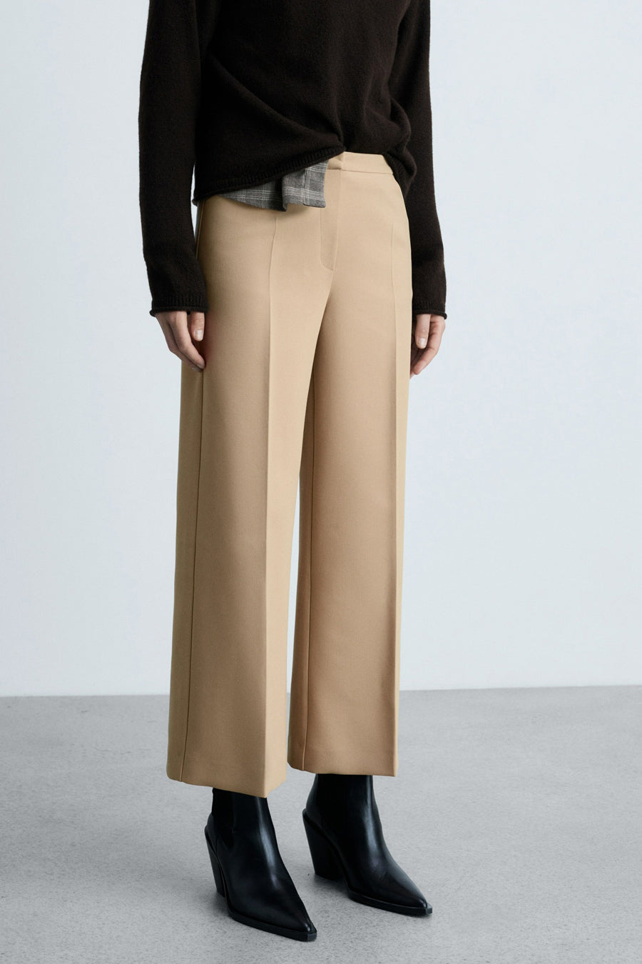 Beige broek van MANGO, wijde pasvorm, gedragen met een bruine trui en zwarte enkellaarsjes.