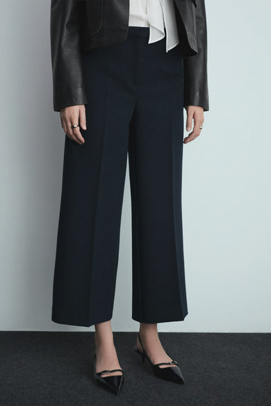 Blauwe broek van MANGO, ruim en hoge taille, gedragen met een zwarte jas en hakken met een riem aan de achterkant.
