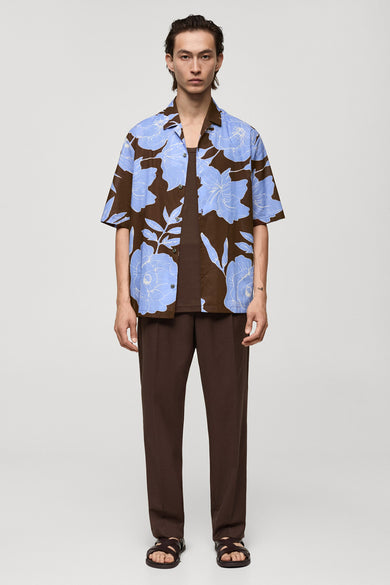 Chemise à manches courtes marron à fleurs bleues de MANGO, portée avec un débardeur et un pantalon marron.