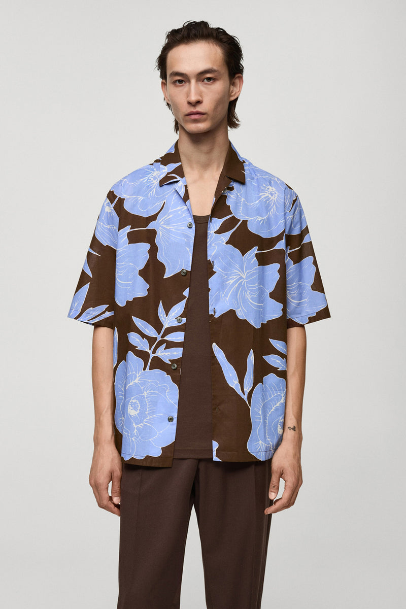 Chemise à manches courtes marron à fleurs bleues de MANGO, portée sur un débardeur marron et un pantalon marron assorti.