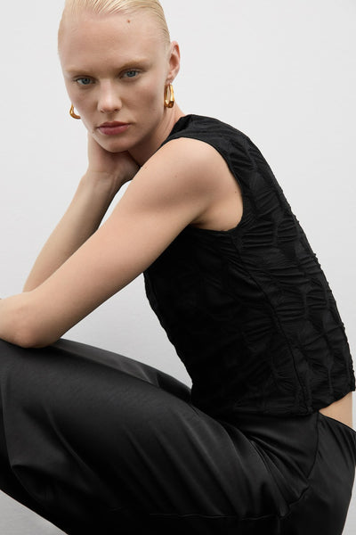 Zwarte blouse met korte mouwen van MANGO, met een wafeltextuur en gedragen met een satijnen zwarte broek.