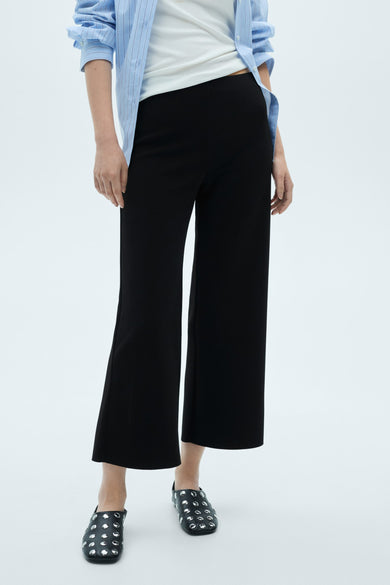 Zwarte broek van MANGO, wijde pasvorm, gedragen met een blauw gestreept overhemd en versierde platte schoenen.