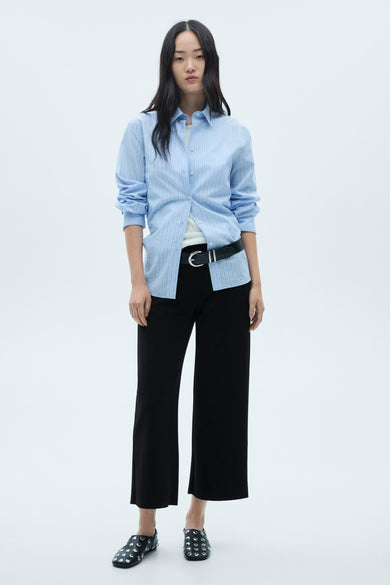 Zwarte pantalon met rechte pijpen van MANGO, gedragen met een zwarte leren riem en platte schoenen met studs.