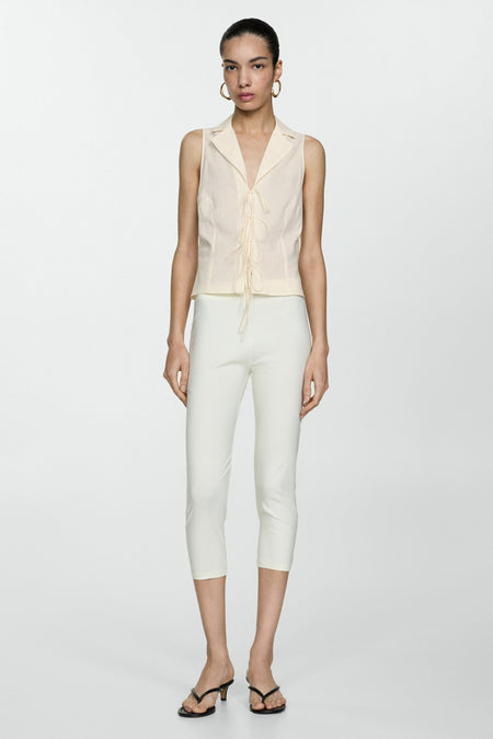 Beige blouse zonder mouwen van MANGO, met een mandje en laagjesl gesloten, gedragen met een wit capri-pantalon.