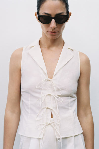Chemisier beige sans manches de MANGO, avec col tailleur et laçage décoratif sur le devant.