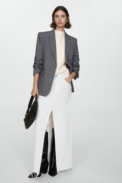 Pull à col rond blanc de MANGO, porté avec une jupe longue fendue et des bottes en cuir noires.
