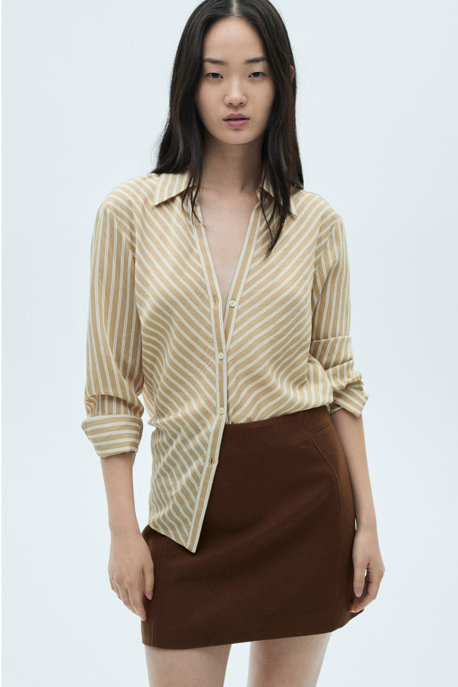 Korte bruine rok van MANGO, met een rechte pasvorm en zachte textuur, gedragen met een beige en witte gestreepte blouse.