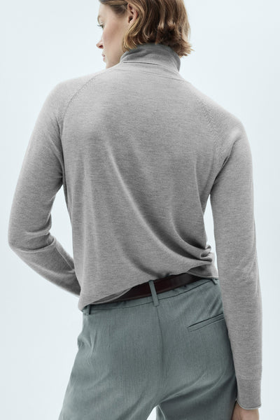Beige coltrui van MANGO, van achteren gezien, gedragen met een grijze broek en een bruine riem.