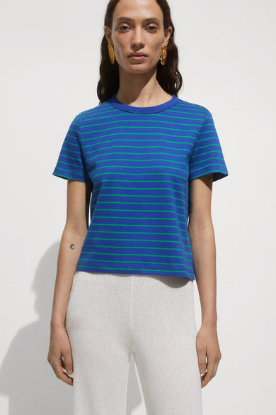 T-shirt bleu à rayures vertes de MANGO, porté avec un pantalon blanc texturé et des boucles d'oreilles dorées.