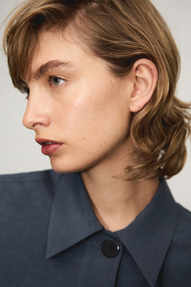 Chemisier bleu à manches courtes de MANGO, avec un bouton noir et une texture lisse.
