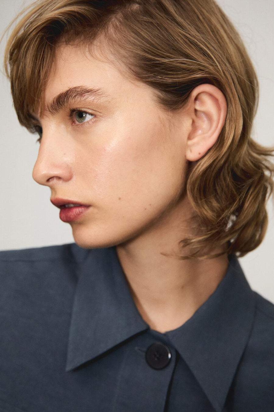 Chemisier bleu à manches courtes de MANGO, avec un bouton noir et une texture lisse.

