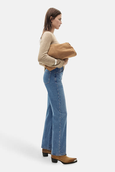 Rechte spijkerbroek in middinblauw denim van MANGO, met klinknagels aan de zijkanten, gedragen met een beige trui en bruine enkellaarsjes.